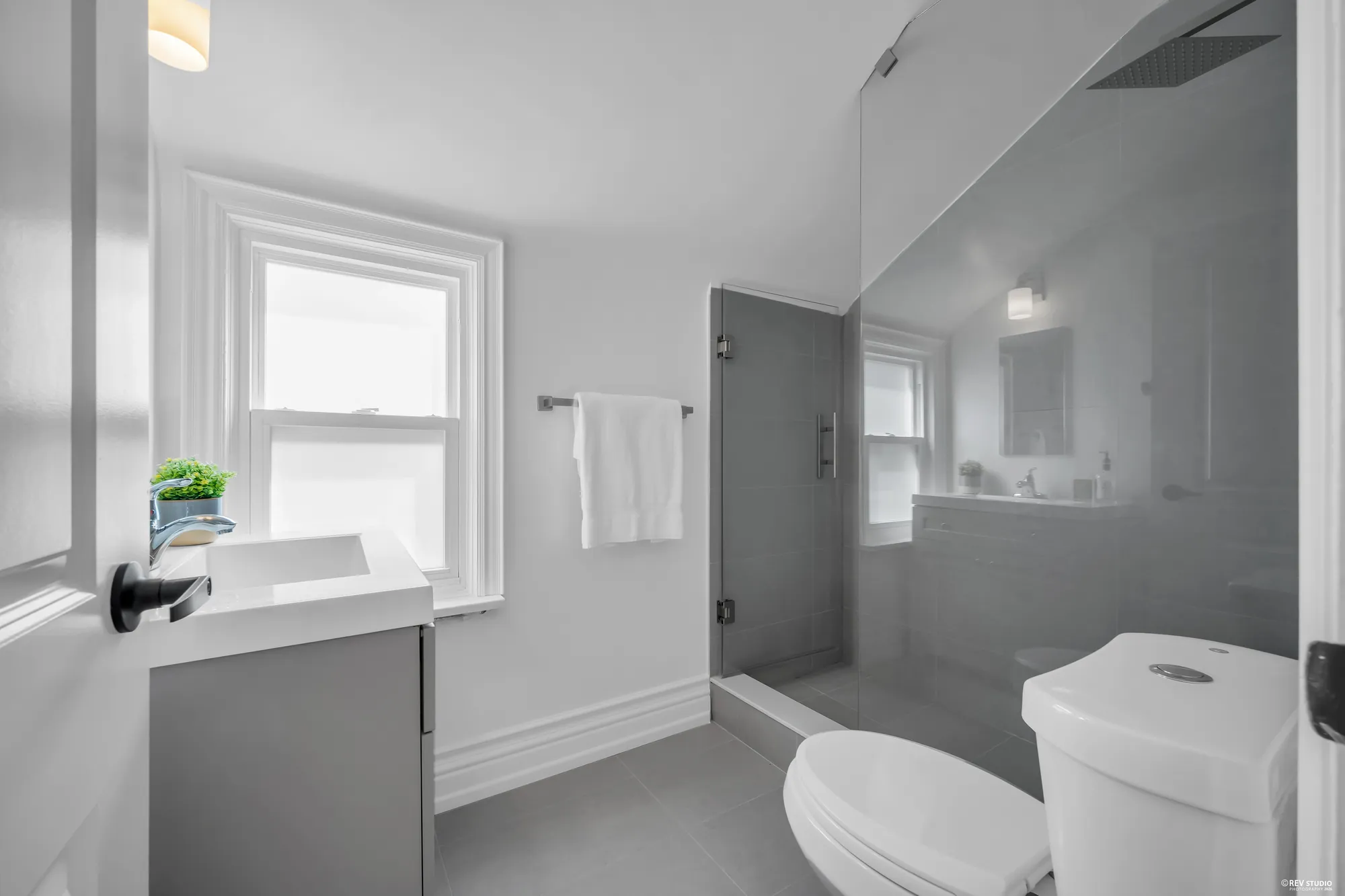 The upstairs bathroom with a glass shower, a vanity and a window