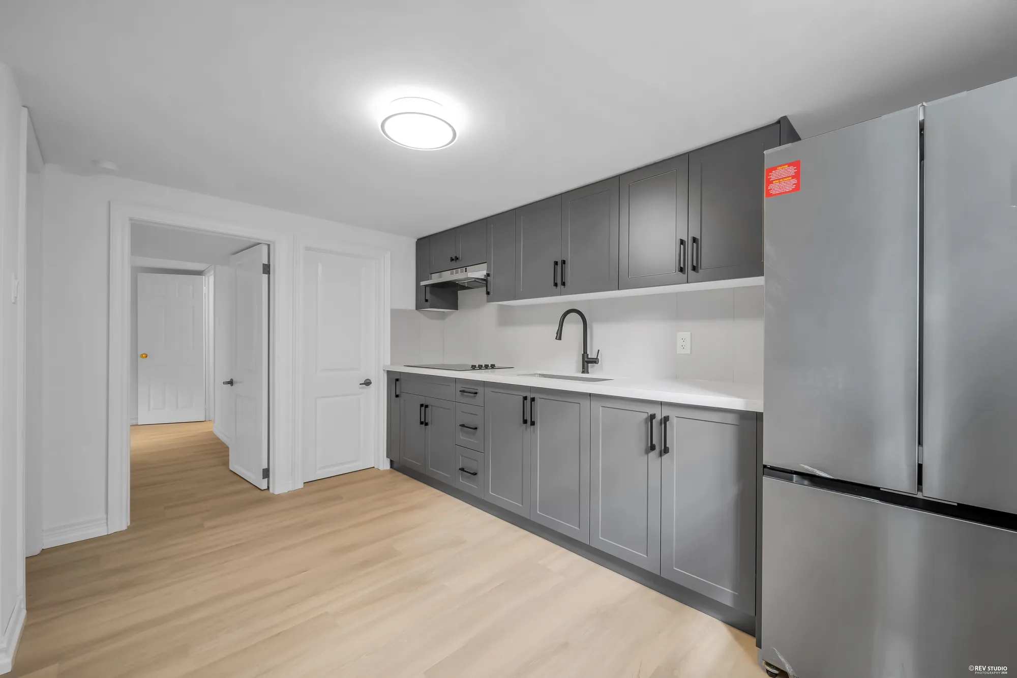 The second kitchen on the lower level with grey cabinets and a stainless refrigerator